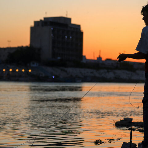 An Iraqi boy catches fish in the Tigris River in central Baghdad as the sun sets, on April 15, 2025.