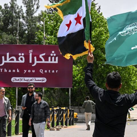 A man carries the Syrian and the Saudi flags past a billboard thanking Qatar, in Damascus, on May 14, 2025.