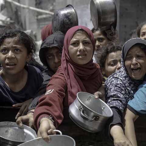 Women and children extend their arms with empty pots in Jabalia Refugee Camp, Gaza City, Gaza, on May 19, 2025.