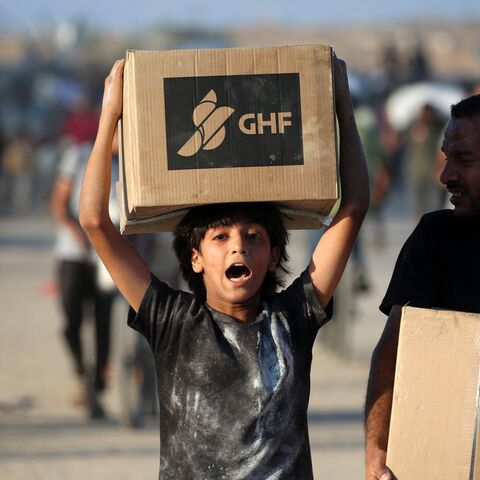 People carrying aid parcels walk along the Salah al-Din road near the Nusseirat refugee camp in the central Gaza Strip, used by food-seeking Palestinians to reach an aid distribution point set up by the privately run Gaza Humanitarian Foundation (GHF, on June 25, 2025.