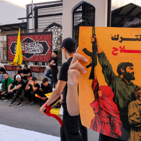TOPSHOT - A person holds a sign with the Arabic slogan "we will not relinquish arms" as Lebanese Shiite Hezbollah supporters take part in a ceremony during the peak of Ashura, a 10-day period commemorating the seventh century killing of Prophet Mohammed's grandson Imam Hussein, in Beirut's southern suburbs on July 6, 2025. (Photo by ANWAR AMRO / AFP) (Photo by ANWAR AMRO/AFP via Getty Images)