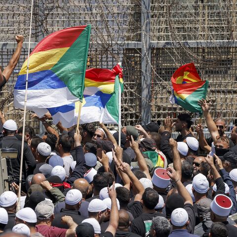 Members of the Druze community demonstrate before Israeli forces by the barbed-wire fence separating the Israeli-annexed Golan Heights and Syria near Majdal Shams, on July 16, 2025. 
