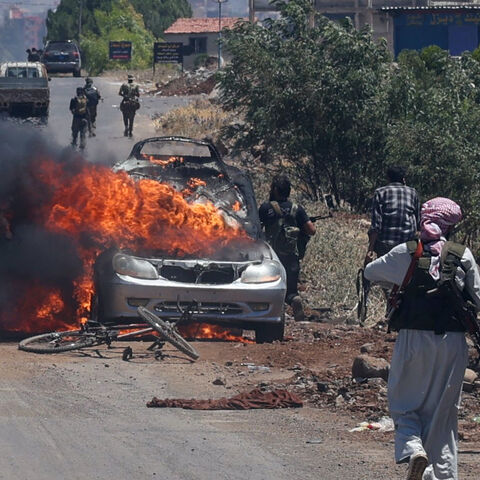 Bedouin and tribal fighters deploy as a car burns at the western entrance of Syria's Druze heartland of Suwayda on July 18, 2025. 