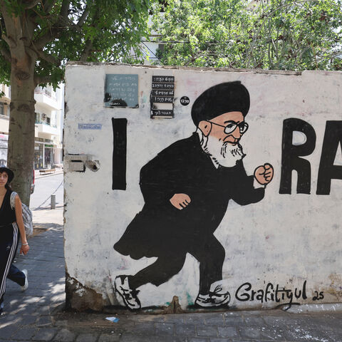 People walk past a mural drawn by the "Grafitiyul" graffiti art group depicting Iran's Supreme Leader Ayatollah Ali Khamenei, on a street in the Israeli coastal city of Tel Aviv on July 22, 2025. (Photo by JACK GUEZ / AFP) / RESTRICTED TO EDITORIAL USE - MANDATORY MENTION OF THE ARTIST UPON PUBLICATION - TO ILLUSTRATE THE EVENT AS SPECIFIED IN THE CAPTION (Photo by JACK GUEZ/AFP via Getty Images)