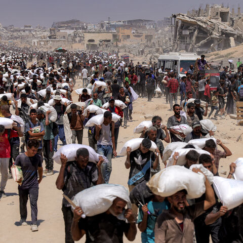 TOPSHOT - People walk with sacks of flour delivered after trucks carrying humanitarian aid entered northern Gaza on July 27, 2025 coming from the Zikim border crossing. (Photo by BASHAR TALEB / AFP) (Photo by BASHAR TALEB/AFP via Getty Images)