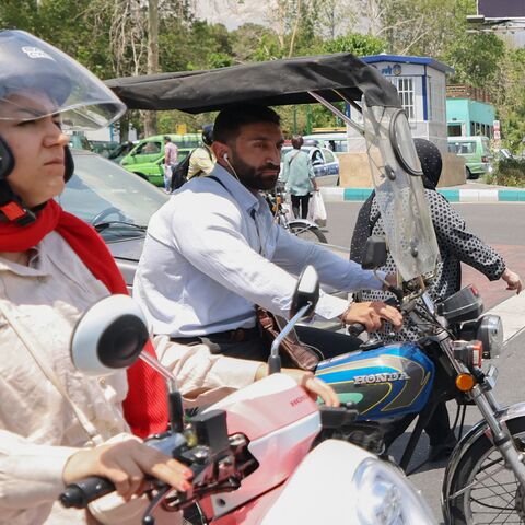 A man and a woman ride their motorcycles past a billboard in the background bearing a portrait of Iran's late President Ebrahim Raisi in central Tehran, on May 21, 2024.