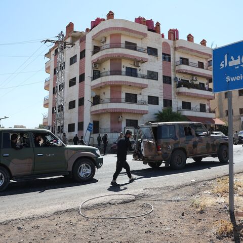 A convoy of Syrian military and security forces passes a sign for Sweida city on July 15, 2025, near Sweida, Syria.