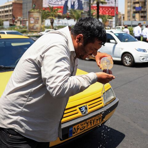 An Iranian taxi driver cools down by splashing water on his face on a street amid soaring temperatures in Tehran on July 22, 2025. 
