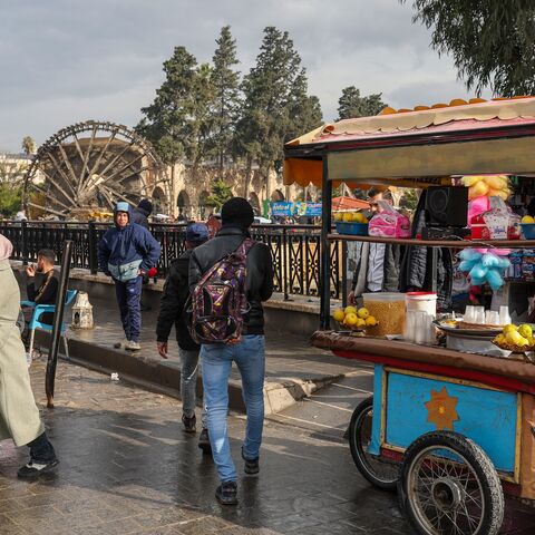 People and street vendors move past one of Hama's landmark historic water wheels on a bridge over the Orontes riverbank in the heart of the central Syrian city on Dec. 30, 2024.