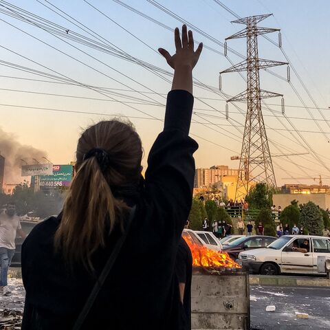 Iranian women without wearing hijab shout slogans while gathering around a burning dumpster during a protest near Punak square, on Oct. 1, 2022