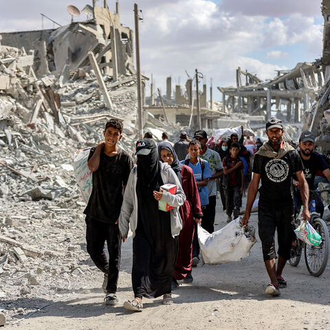 People walk along a destroyed road past heavily-damaged buildings in the centre of Khan Yunis in the southern Gaza Strip on Oct. 10, 2025, as the displaced return to their homes after Israeli forces' withdrawal.