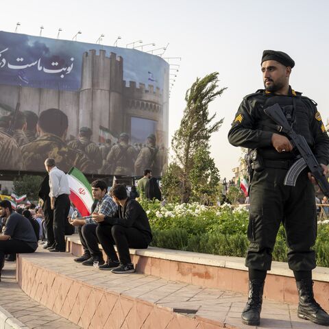 TEHRAN, IRAN - JUNE 24: A Police officer stands guard as demonstrators wave flags and cheer during a gathering to honor Iran’s military forces, following the announcement of a ceasefire between Israel and Iran, on June 24, 2025 in Tehran, Iran. Iranian authorities announced this morning they would agree to a ceasefire with Israel, whose attacks on Iran's military and nuclear sites on June 13 sparked a daily exchange of missiles between the countries. (Photo by Majid Saeedi/Getty Images)