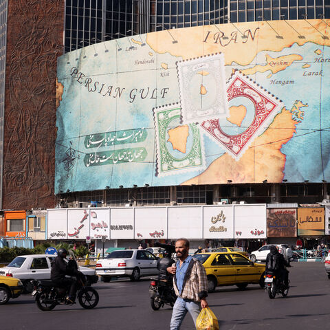 People walk and drive past a billboard covering the facade of a building on Vali-Asr square, depicting as postage stamps the disputed Abu Musa and Greater and Lesser Tunb islands that were seized by Iran in 1971, in Tehran on October 26, 2024. Residents of Tehran awoke and went about their business as planned on October 26 after their sleep was troubled by Israeli strikes that triggered blasts that echoed across the city. (Photo by ATTA KENARE / AFP) (Photo by ATTA KENARE/AFP via Getty Images)