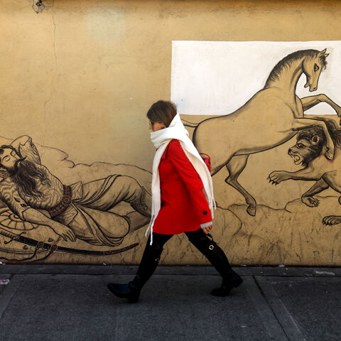 An Iranian woman walks past a mural depicting a scene from the Iranian national epic "Shahnameh" in the capital Tehran on January 6, 2026. Iran's economy has been hit hard by tough international sanctions, with the national currency, the rial, losing more than a third of its value against the US dollar over the past year and inflation in double digits. (Photo by ATTA KENARE / AFP via Getty Images)