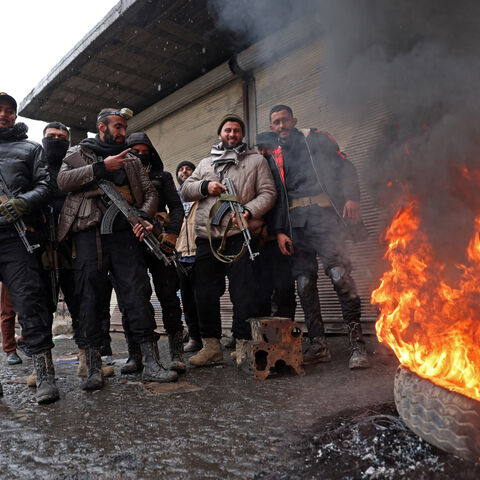Syrian government troops stand guard next to a burning tyre along a street of Tabqa, in Raqa province, on the southwestern banks of the Euphrates on Jan. 18, 2026. 