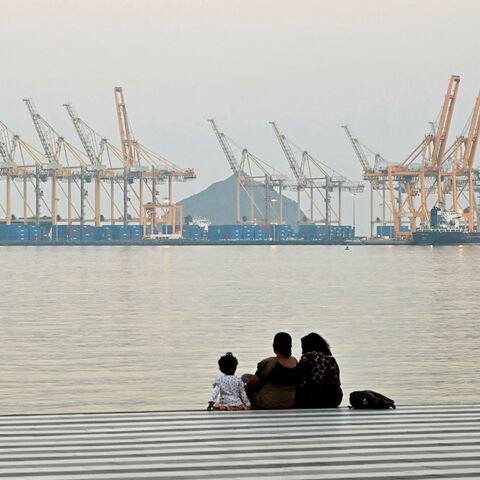 A family sits against the backdrop of a dockyard in Khor Fakkan in the Gulf emirate of Sharjah, off the coast of the Gulf of Oman, on Feb. 25, 2026. 