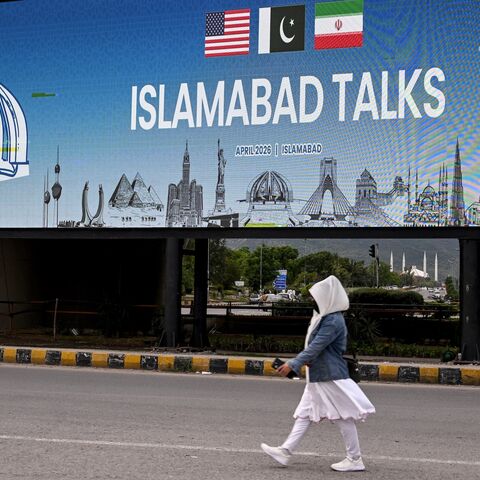 A woman walks past a digital screen displaying news of US-Iran peace talks along a road in Islamabad on April 10, 2026. 