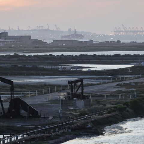 A pumpjack stands idle in the Huntington Beach oil field, with port cranes visible in the distance, on April 23, 2026, in Huntington Beach, California.