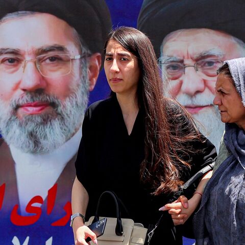 Women walk past a large banner depicting Iran's current supreme leader, Mojtaba Khamenei, and his predecessor and late father, Ali Khamenei, along a street in Tehran on May 6, 2026.