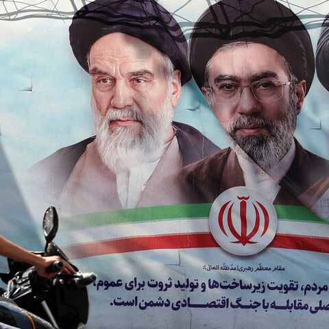 An Iranian man rides his motorbike past a billboard on May 28, 2026.