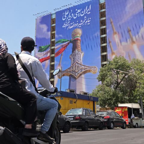 Motorists ride past a giant banner depicting Iranian missiles and a sword belonging to Imam Ali, the first Imam of the Shiites, at the Vanak Square in Tehran on June 10, 2026. 