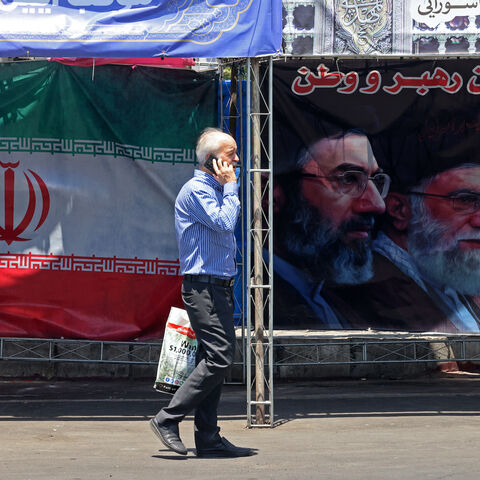 A man walks past Iran's national flag and a banner bearing the images of the late founder of the Islamic Revolution supreme leader Ayatollah Ruhollah Khomeini (R), the late Iranian supreme leader Ali Khamenei and his son, the current supreme leader Mojtaba Khamenei (L), erected along a street at the Vanak Square in Tehran on June 10, 2026.