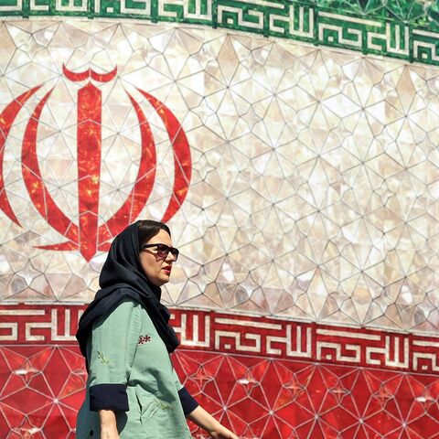 A woman walks past a billboard displaying Iran's national flag at Enghelab Square in Tehran on June 14, 2026.