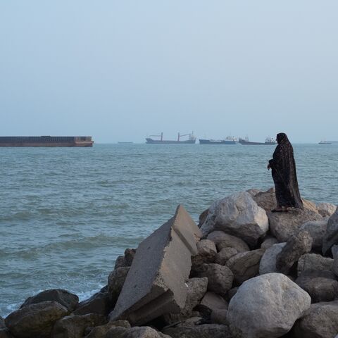 A women stands overlooking the water as ships are seen anchored in the Strait of Hormuz on Aug. 10, 2026, off the coast of Bandar Abbas, Iran.