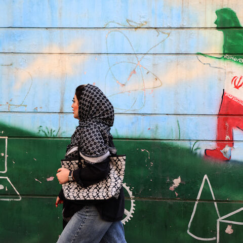 A woman walks past a wall painting in the colours of the Iranian flag in Tehran on February 25, 2026. (Photo by ATTA KENARE / AFP via Getty Images)
