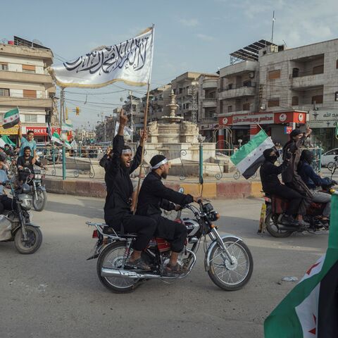 Demonstrators ride through a street while waving Syrian flags