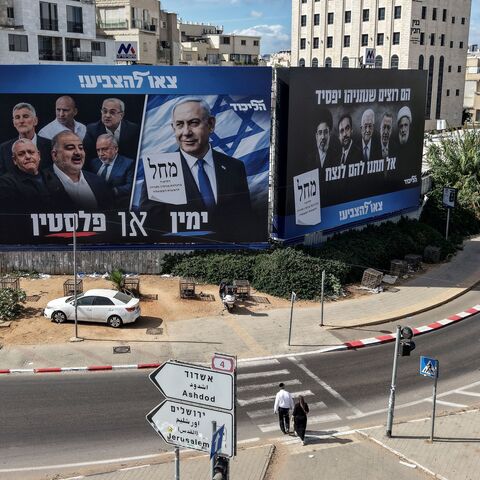 Pedestrians cross a street in front of a banner featuring Israeli Prime Minister Benjamin Netanyahu