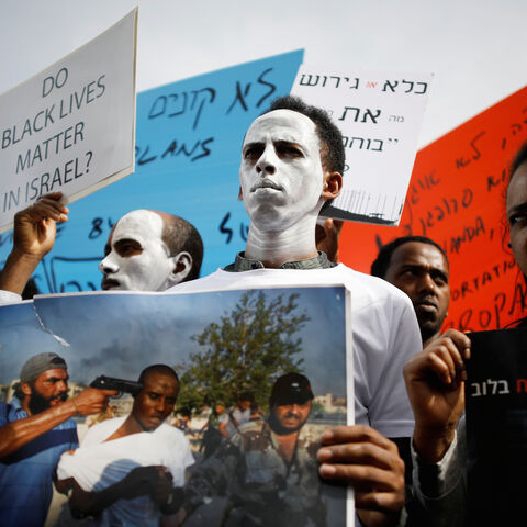 African migrants painted in white hold signs during a protest against the Israeli government's plan to deport part of their community, in front of the Rwandan embassy in Herzliya, Israel February 7, 2018. REUTERS/Amir Cohen - RC1E0E1052F0