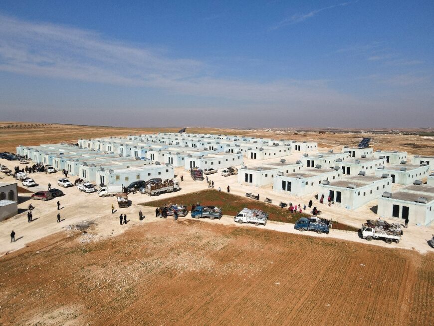 Internally displaced Syrians arrive with their belongings in a convoy of trucks at their new housing complex