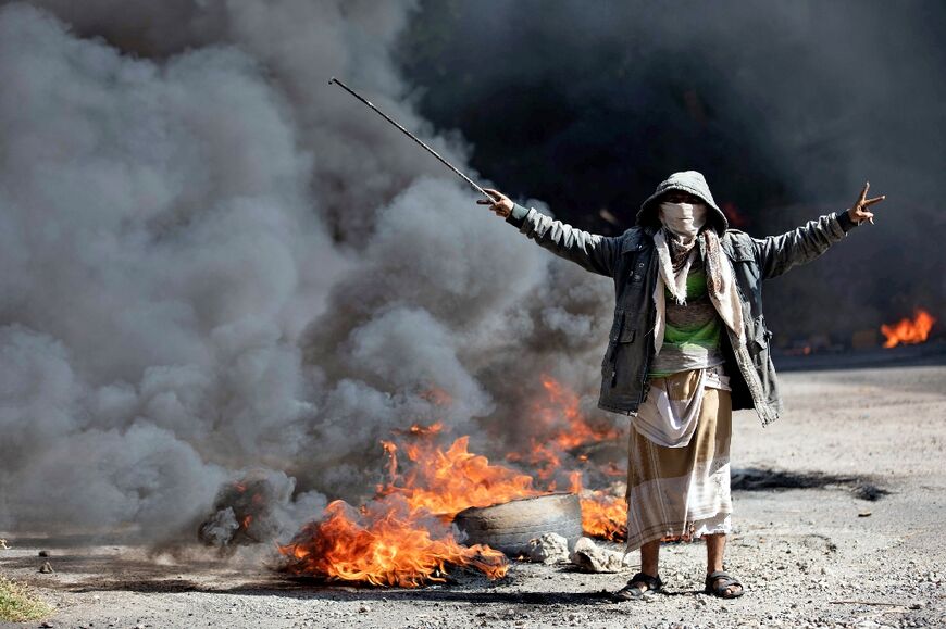 A man flashes the V-for-victory sign next to burning tyres during protests in Yemen's third city of Taez on September 27, 2021