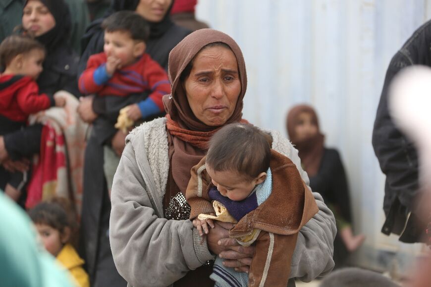 A Syrian woman carries a child across a regime-controlled corridor in 2018