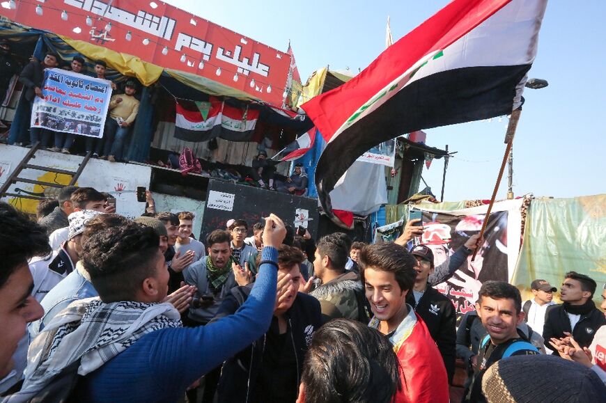 Iraqi anti-government protesters chant and wave a national flag in Baghdad's Tahrir square on December 22, 2019 calling for an overhaul of a regime they deem corrupt and inefficient