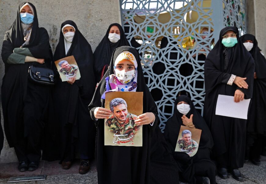 Mourners carry pictures of other 'martyrs' killed during Iranian operations overseas as they join the large crowds on the streets for Khodai's funeral procession