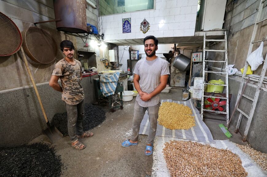 Roaster Majid Ebrahimi (R) and a worker pose for a picture in front of their roasting machine in Tehran's Grand Bazaar