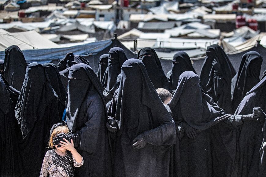 Women and a child queue to receive aid at the Kurdish-run al-Hol camp for relatives of suspected Islamic State group fighters in Syria