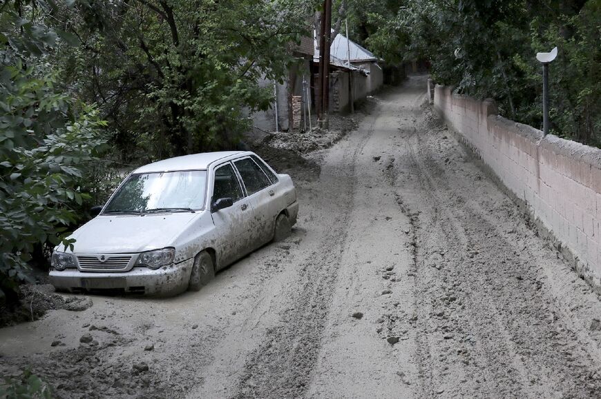 A car partially buried in mud on a road in the Firouzkouh area 