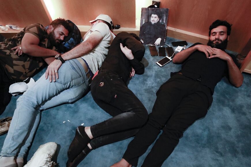 Supporters of Iraqi cleric Moqtada Sadr rest beside his picture after occupying parliament, where they vow to remain