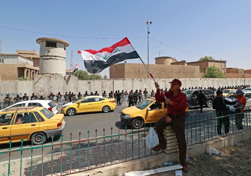 A protester waves an Iraqi national flag as security forces stand guard outside the Turkish visa office in Baghdad during a demonstration against the deadly attack in Kurdistan