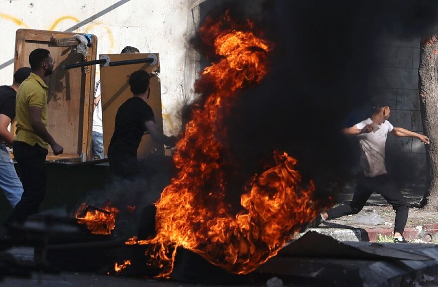 Palestinian protesters use makeshift shields for protection as they hurl stones at Israeli troops who entered Nablus, the main city in the northern West Bank