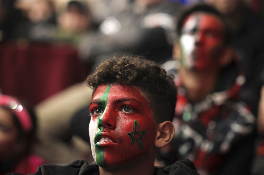 Palestinian football fans with faces painted in the colours of the national and Moroccan flags watch the Qatar 2022 World Cup on December 10