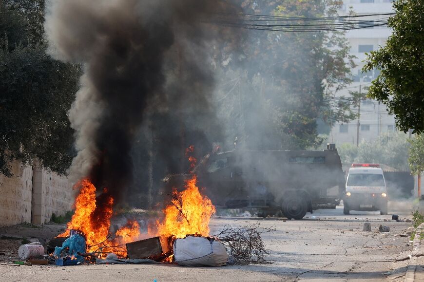 An ambulance drives past an Israeli military vehicle near a burning street barricade in the ocupied West Bank city of Jenin on January 26, 2023