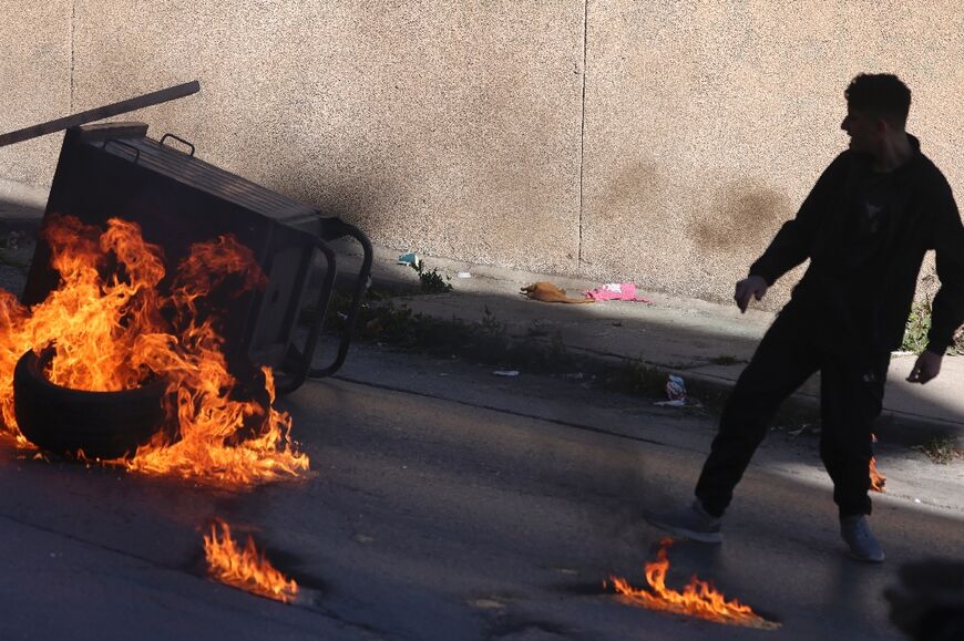 A Palestinian throws a tyre onto a fire as they block a road during a raid by Israeli soldiers in Nablus 