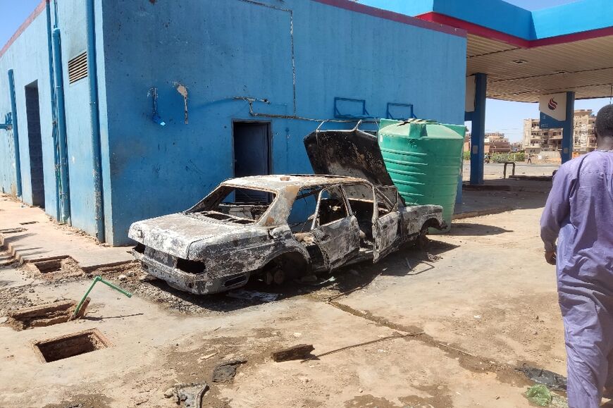 A man walks toward a charred car at a looted petrol station in southern Khartoum