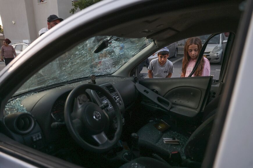 Children look at a damaged car in the southern Israeli city of Sderot