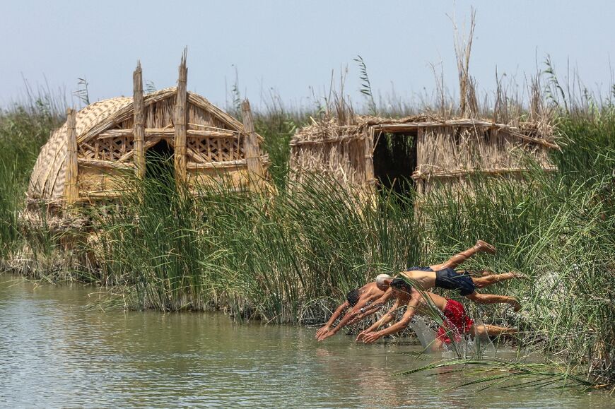 Iraqi Marsh Arabs jump into the water in Chibayish to cool off, their traditional reed homes in the background