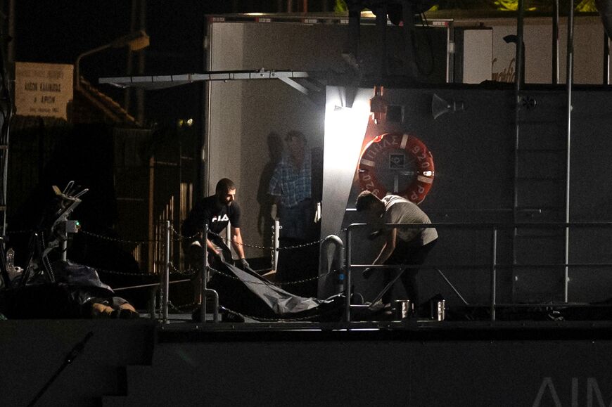 Men carry bodybags from a coast guard vessel to a refrigerated truck at the port in Kalamata, Greece